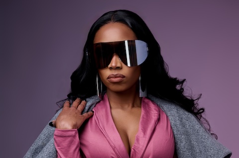 Crystal wearing a grey trench coat with pink underneath and highly stylized sunglasses